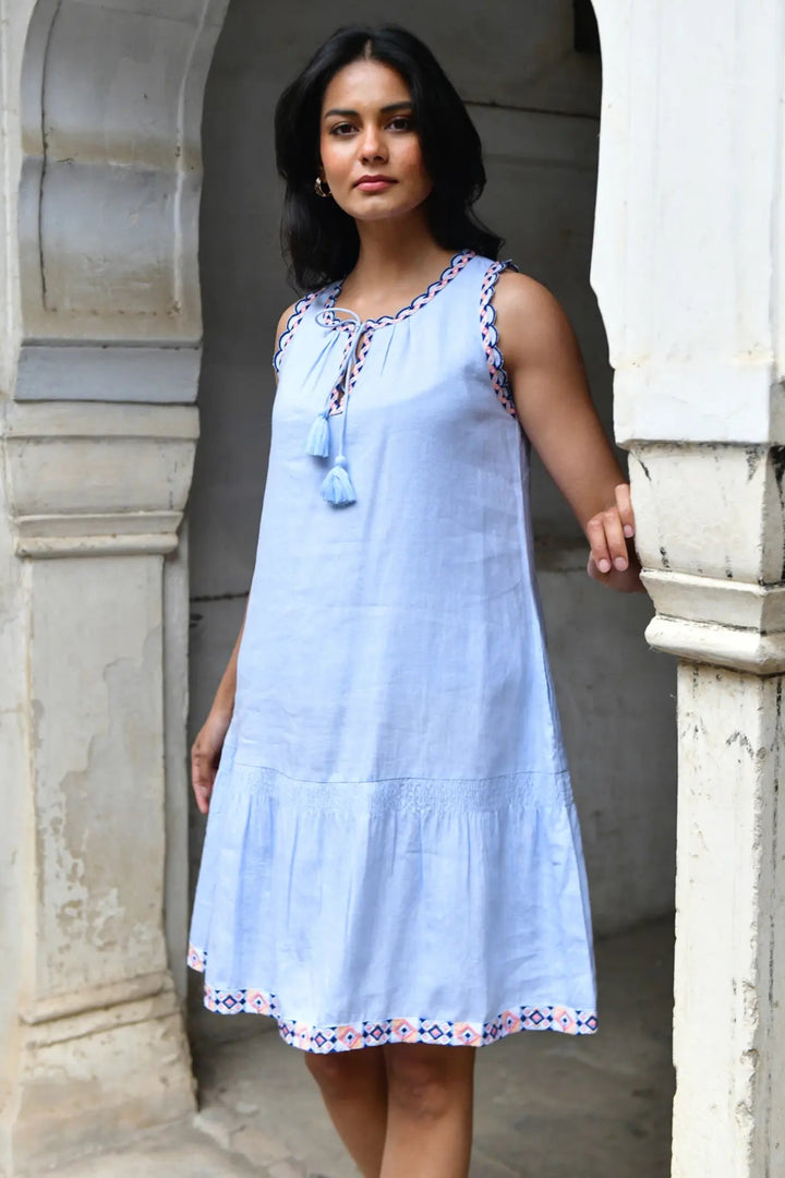Woman wearing a light blue dress with floral details standing in an archway.