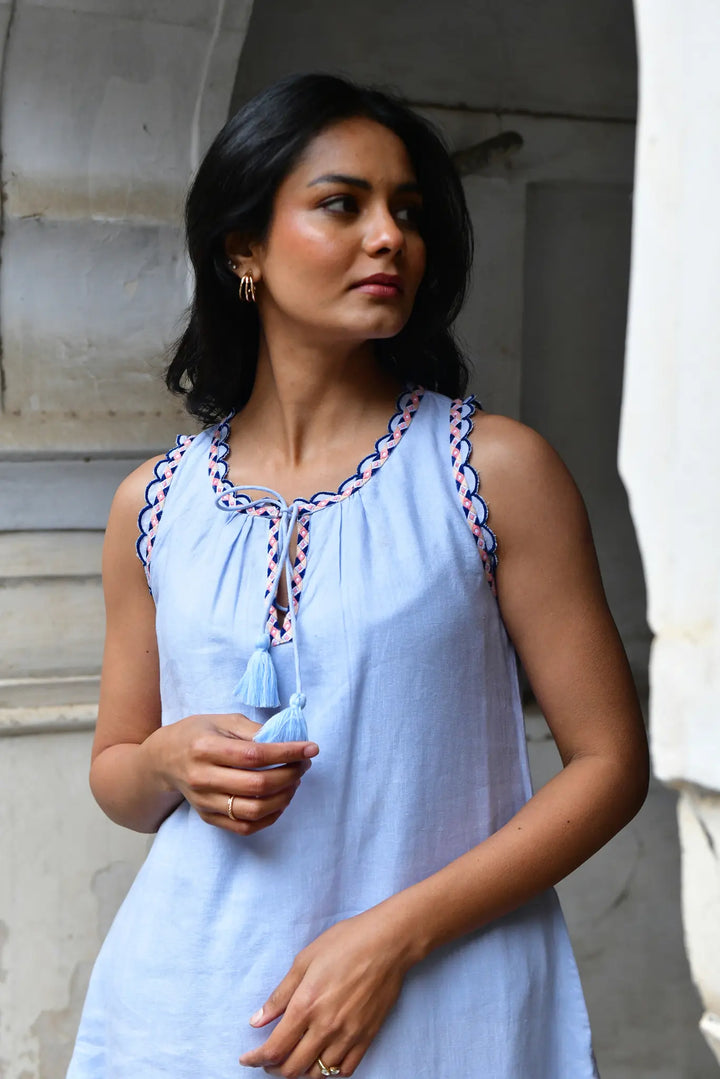Woman wearing a light blue dress with intricate detailing, standing against a neutral background.