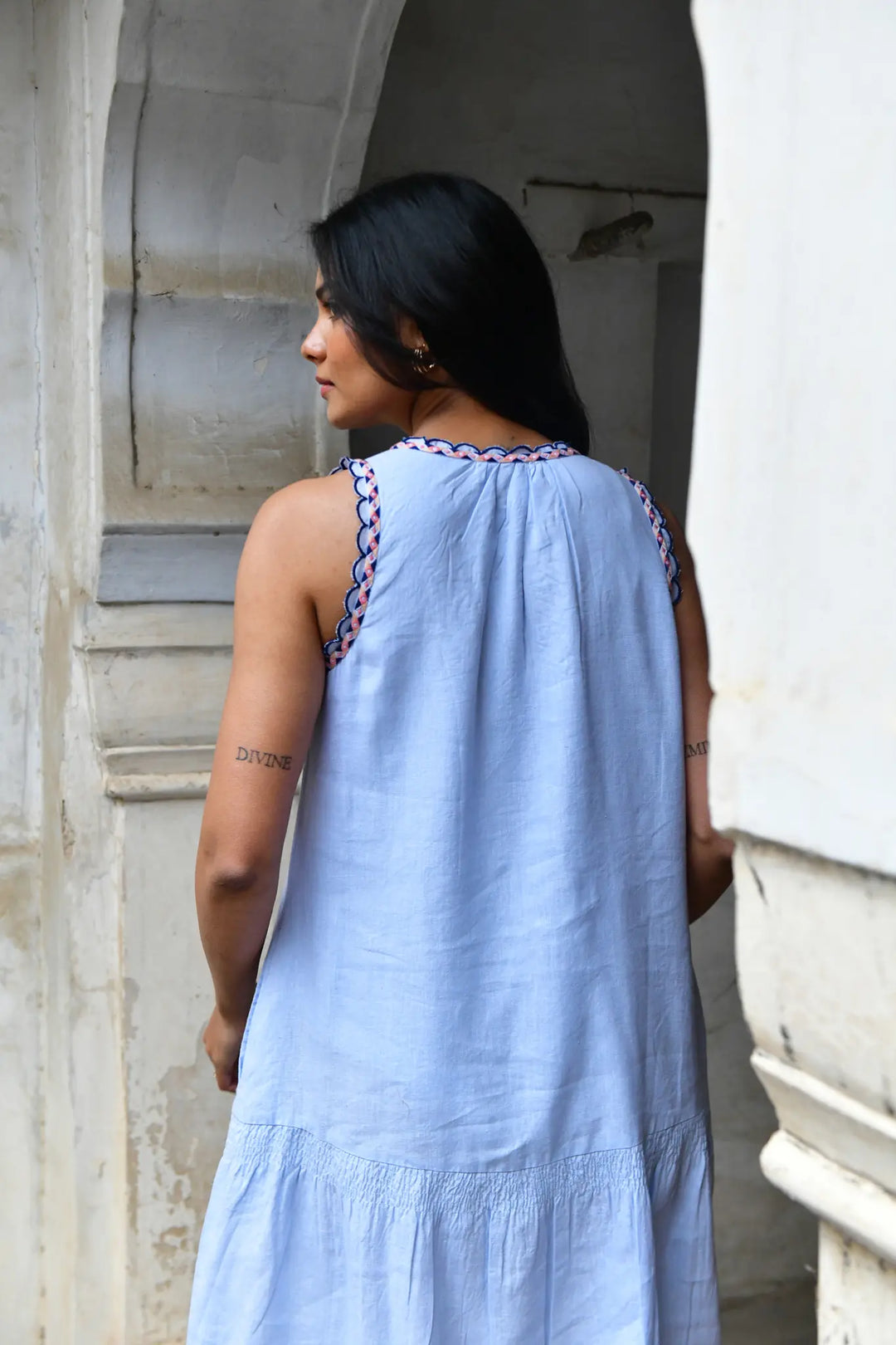Woman wearing a light blue dress with intricate detailing, standing in an architectural setting.