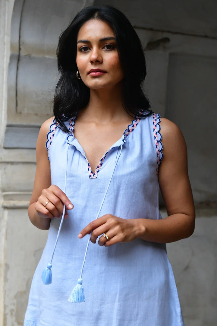 Woman wearing a light blue dress with decorative straps in an outdoor setting
