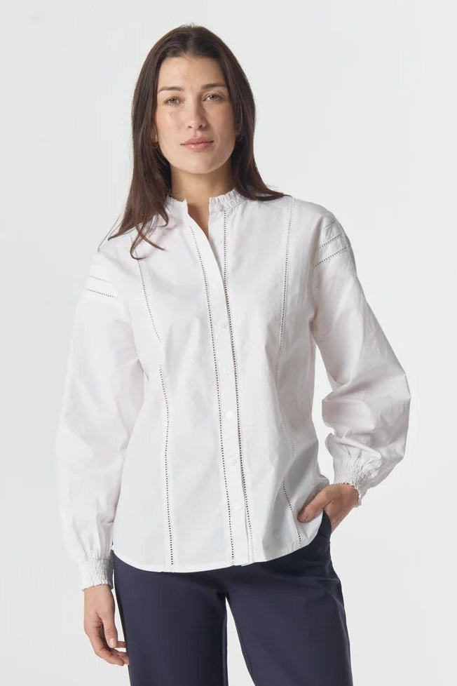 Woman wearing a white blouse and navy pants on a white background