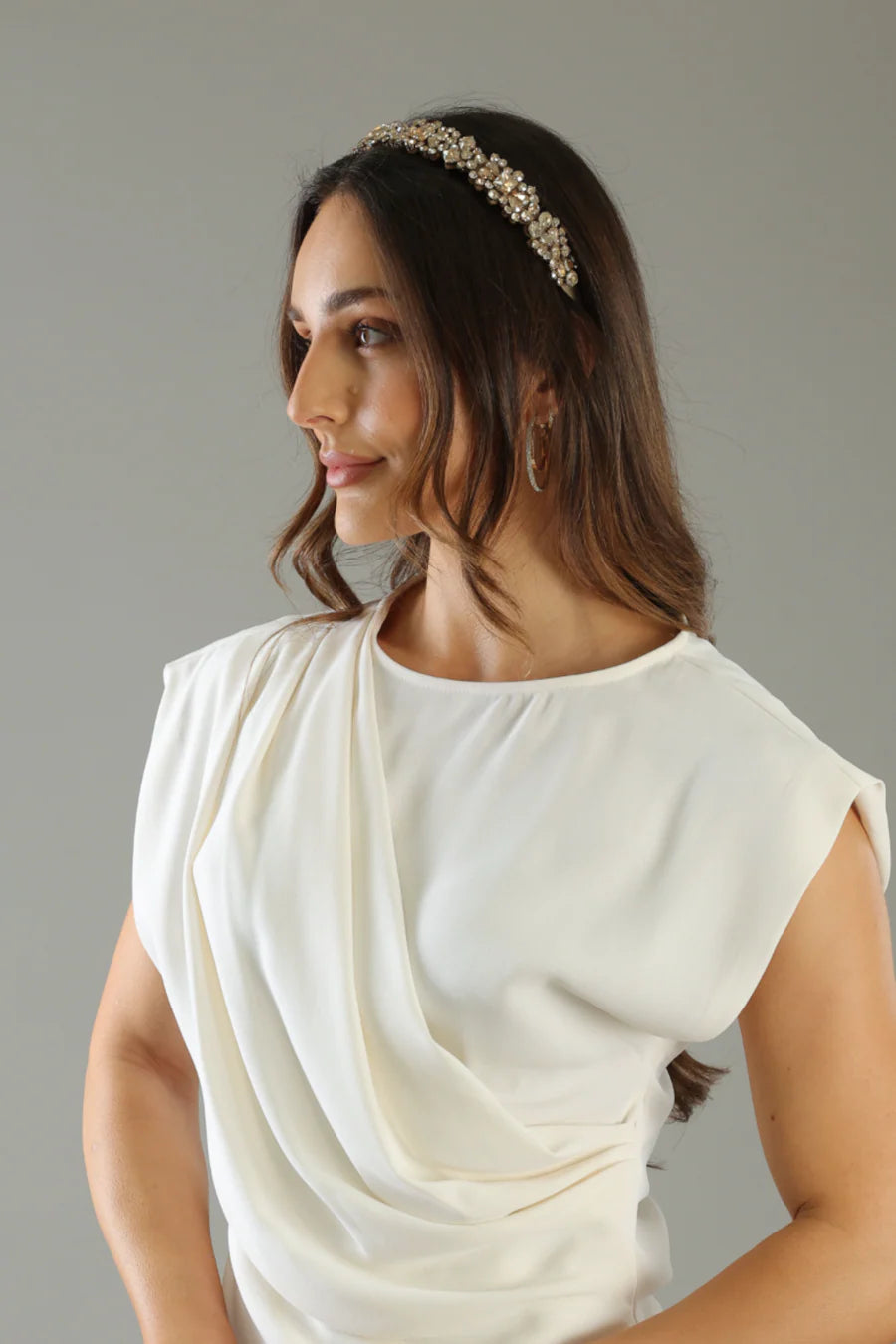 Woman wearing a white top and decorative headband against a neutral background