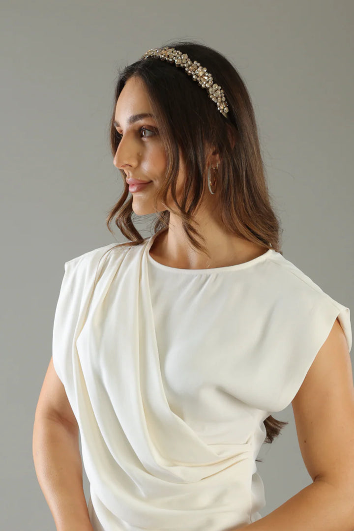 Woman wearing a white top and decorative headband against a neutral background