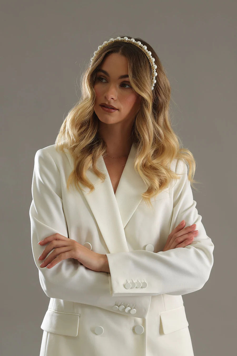 Woman wearing a white bridal outfit with a headband against a neutral background