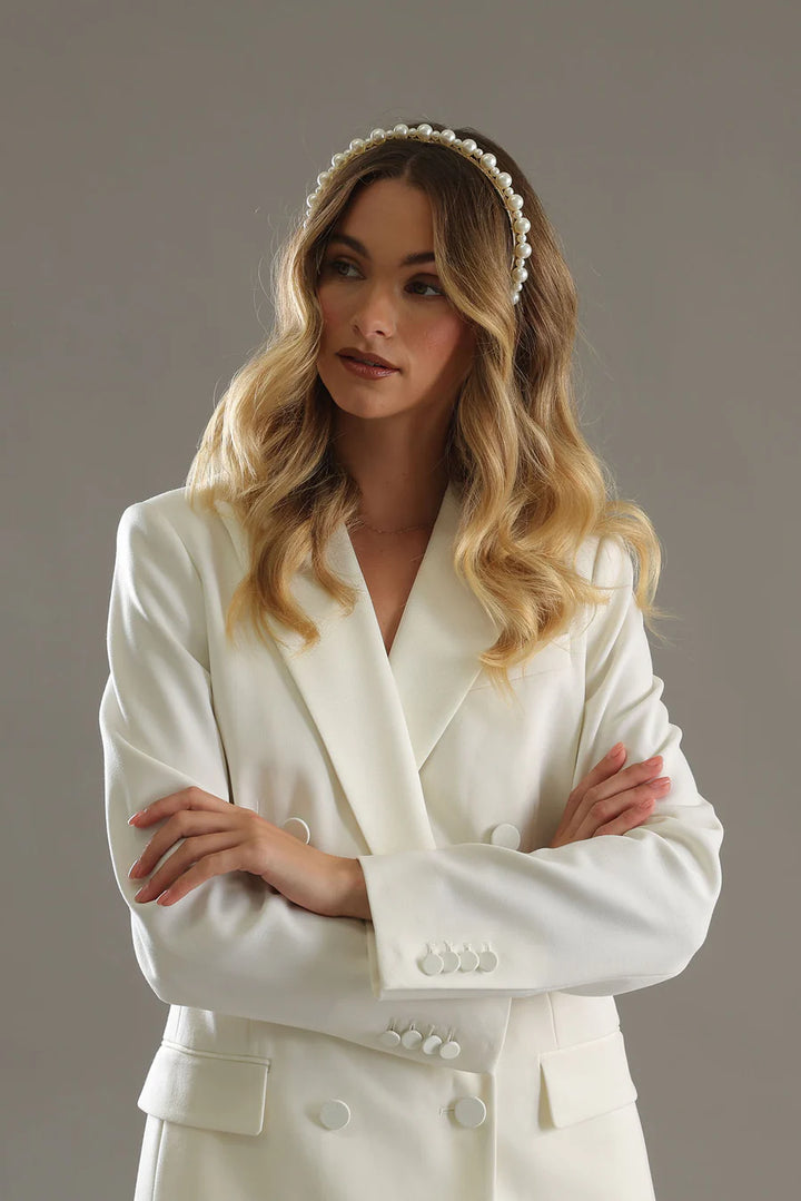 Woman wearing a white bridal outfit with a headband against a neutral background