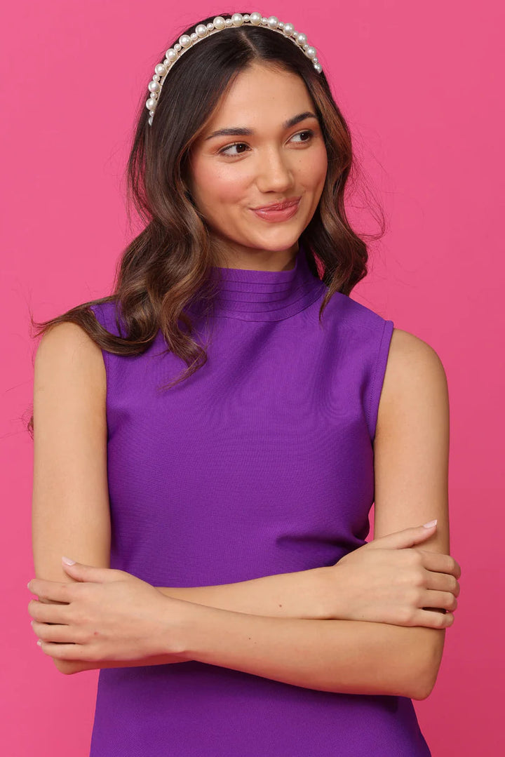 Woman wearing a purple sleeveless top against a pink background