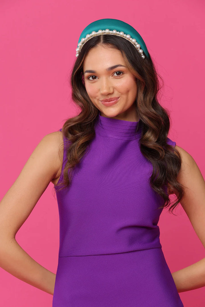 Woman wearing a purple dress and teal headband against a pink background