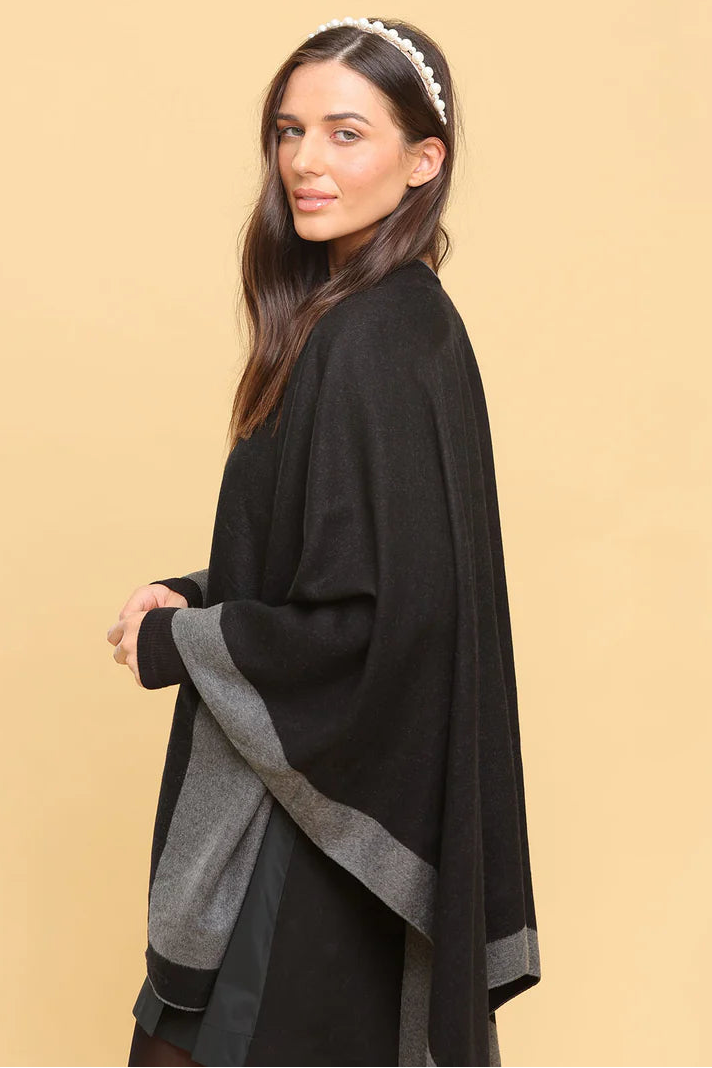 Woman wearing a black and gray poncho against a beige background