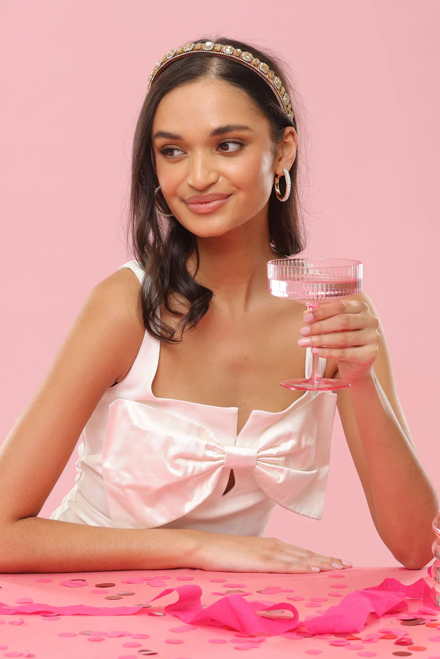 Woman in a satin dress holding a glass with pink confetti on a pink background
