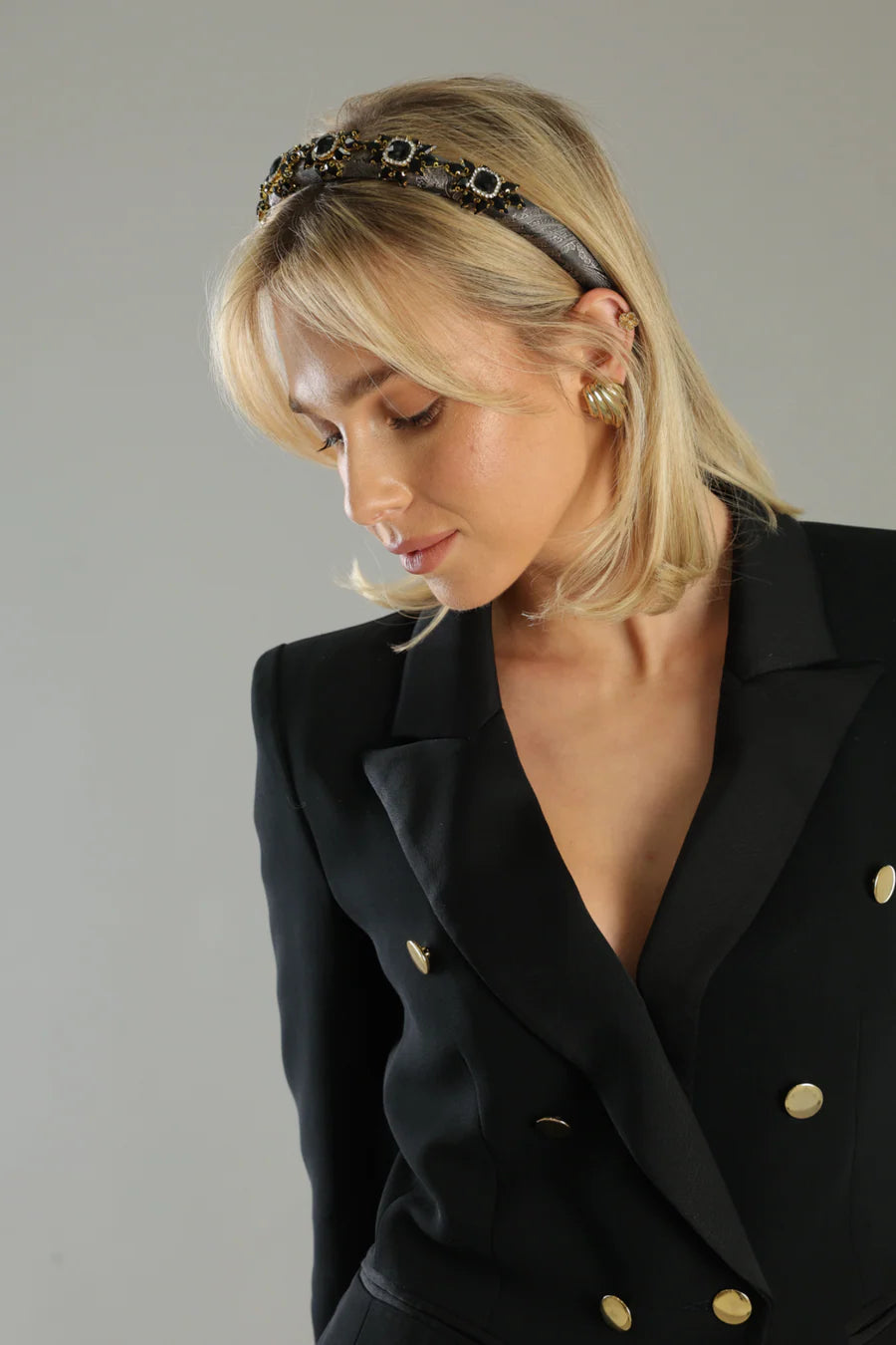 Woman wearing a black blazer with gold buttons against a neutral background