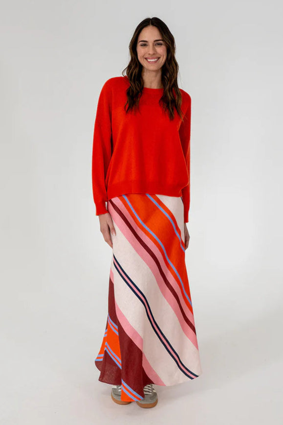 A woman wearing a red long-sleeve knit top with a round neckline, paired with a multicolored skirt.