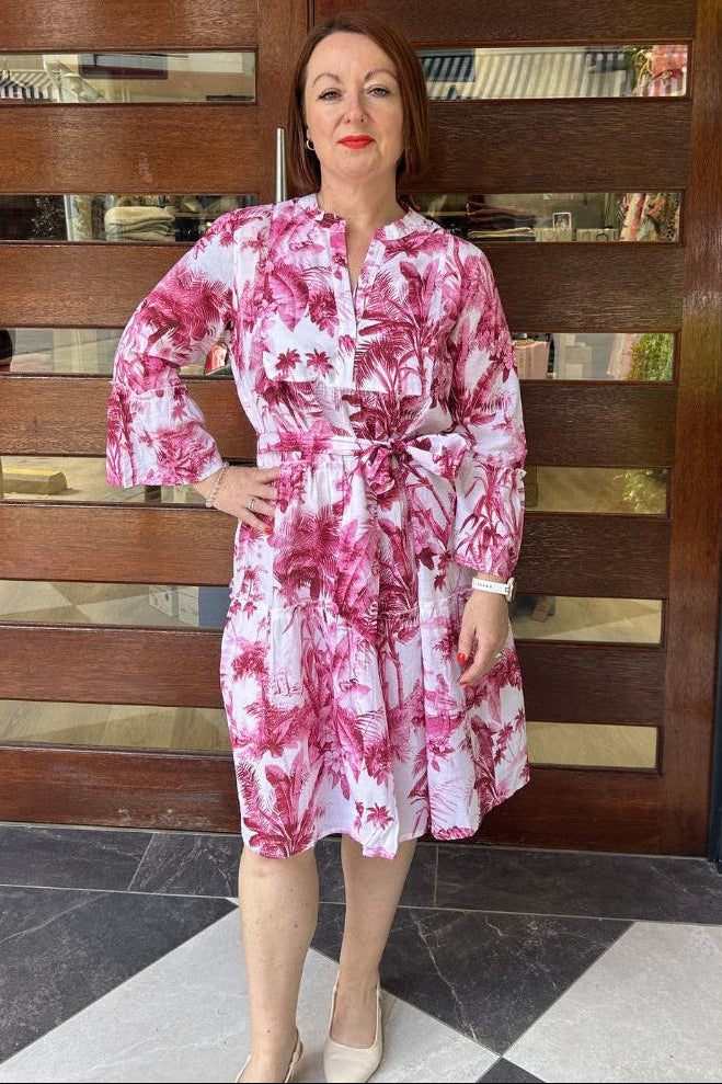 Woman wearing a pink and white floral dress standing in front of a wooden door.