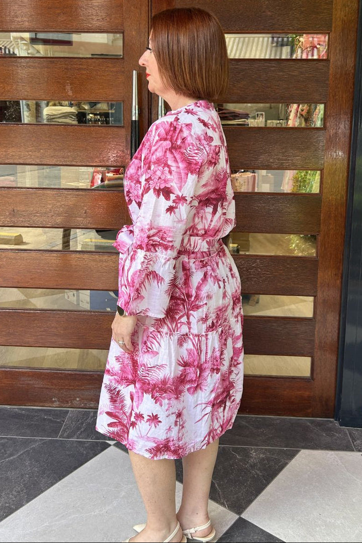 Woman in a pink floral dress standing in front of a wooden door.