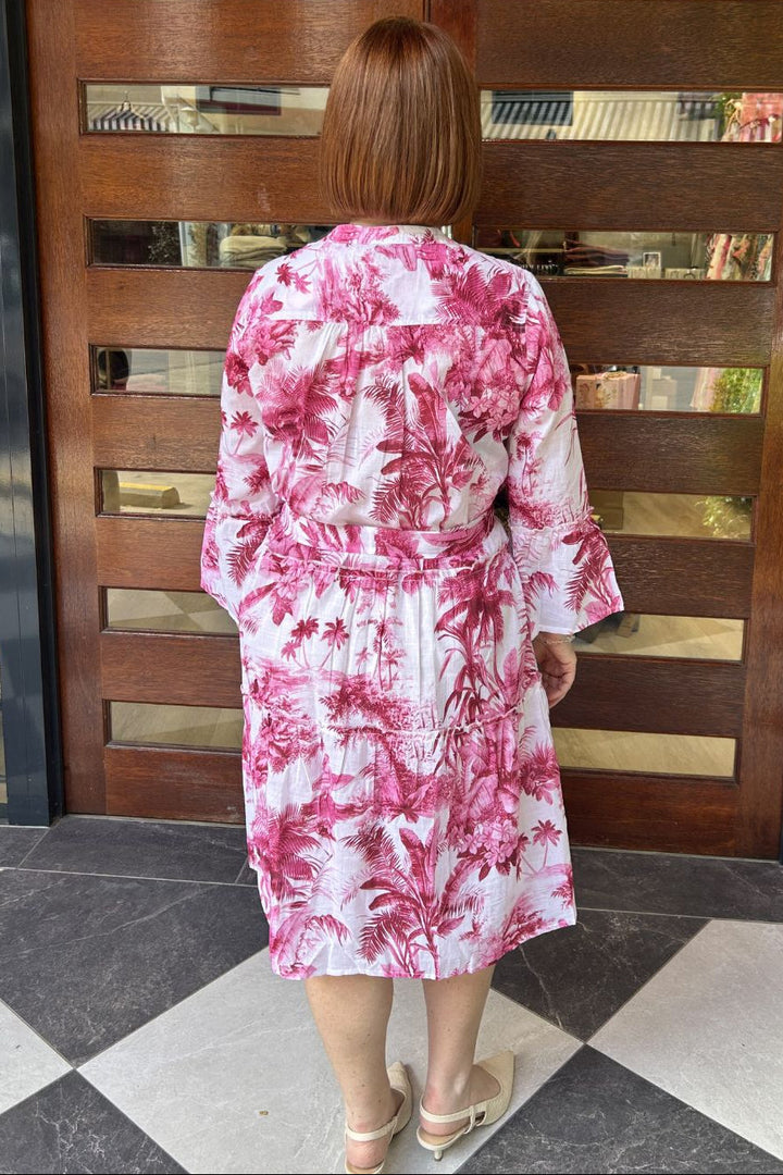 Person wearing a pink and white floral dress standing in front of a wooden door.