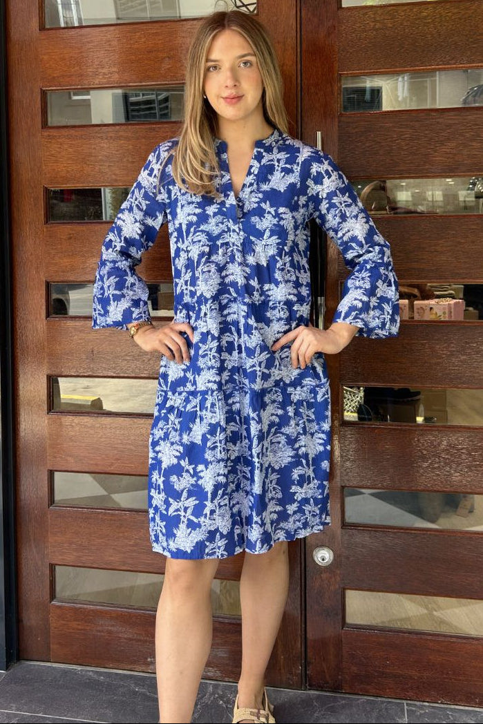 Woman in a blue floral dress standing in front of a wooden door.