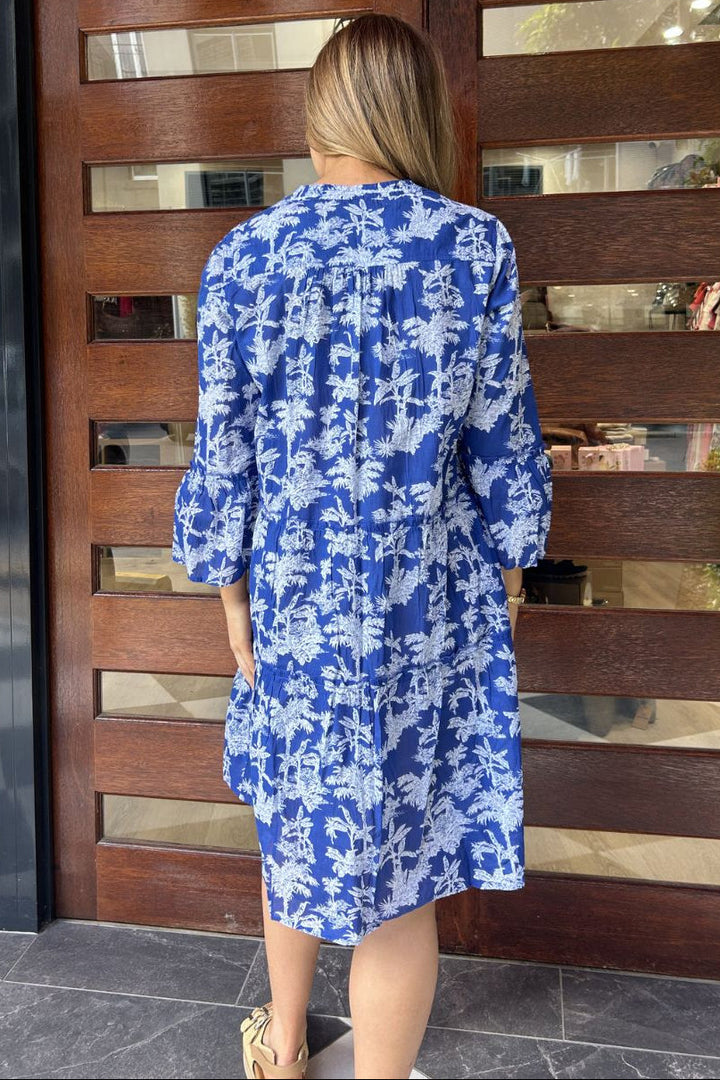Woman wearing a blue floral dress standing in front of a wooden door.