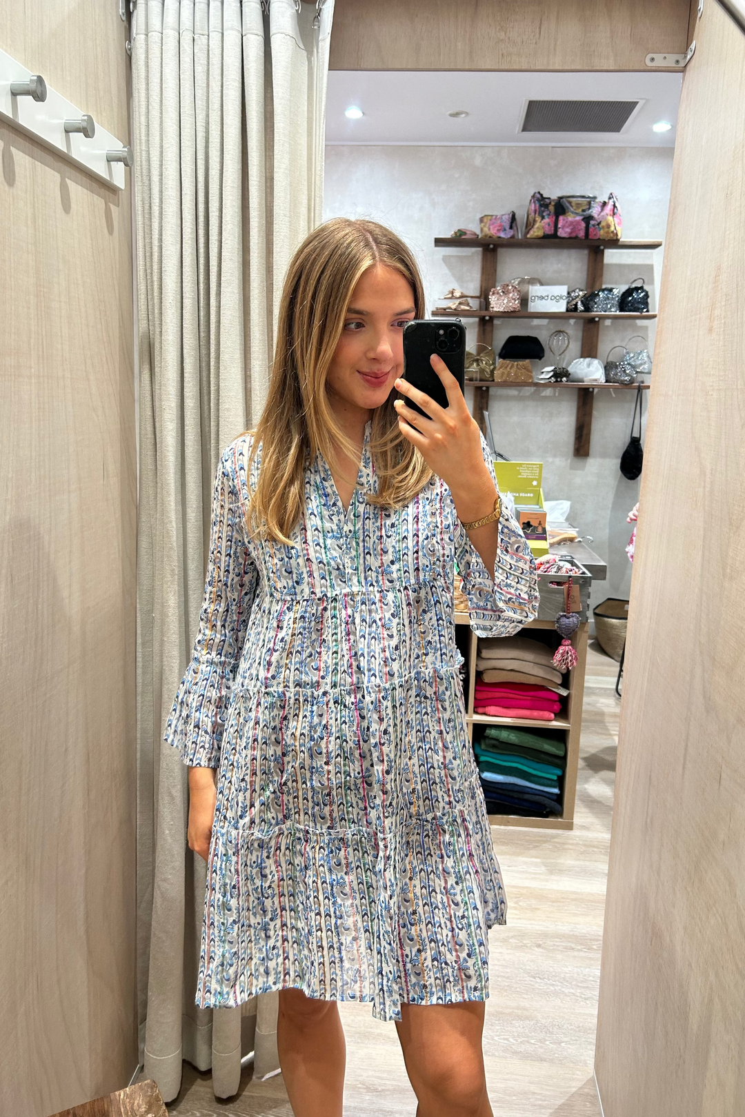 Woman taking a mirror selfie wearing a floral dress in a store.