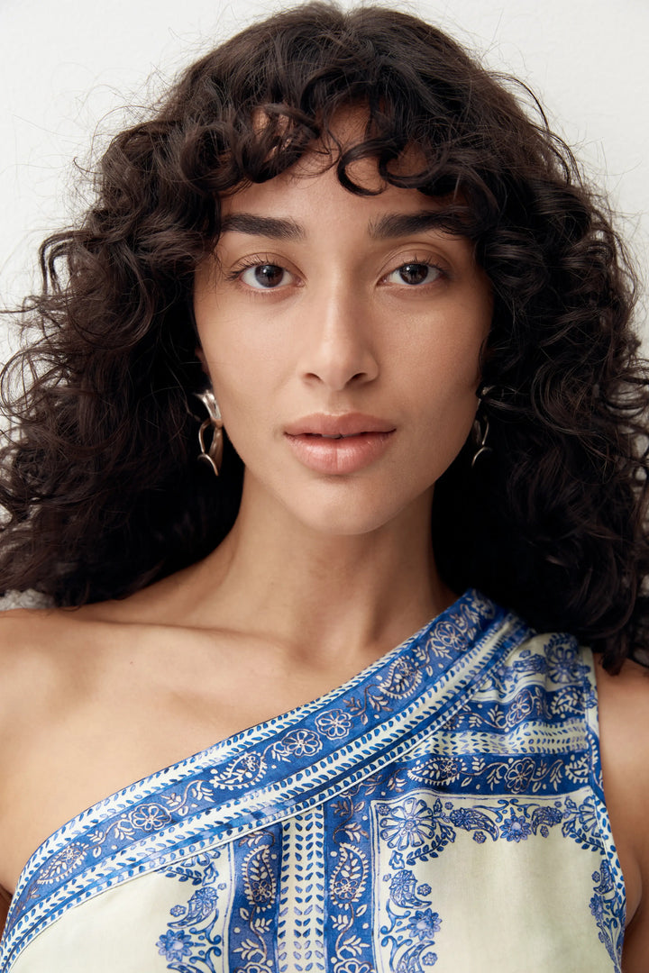 Woman wearing a blue and green patterned saree against a plain background