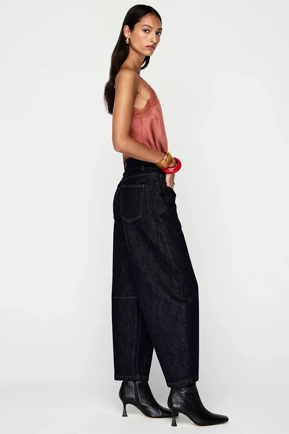 Woman wearing a pink top and black high-waisted jeans on a white background