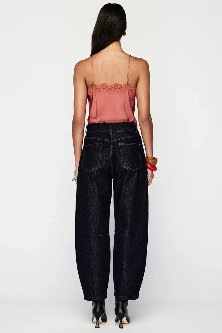 Woman wearing black high-waisted jeans and a pink top on a white background