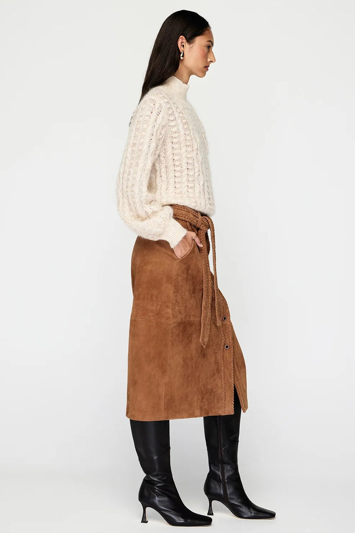 Woman wearing a white sweater, brown suede skirt, and black boots on a white background