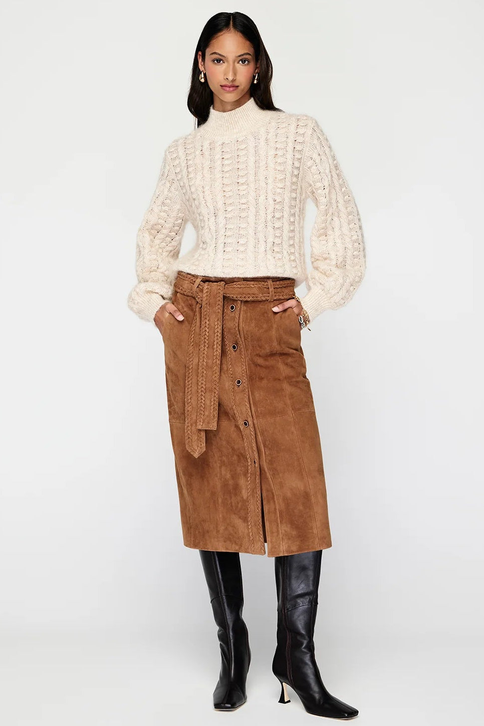 Woman wearing a white ribbed sweater, brown corduroy skirt, and black knee-high boots on a white background