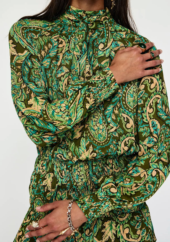 Green and gold patterned dress worn by a person on a white background