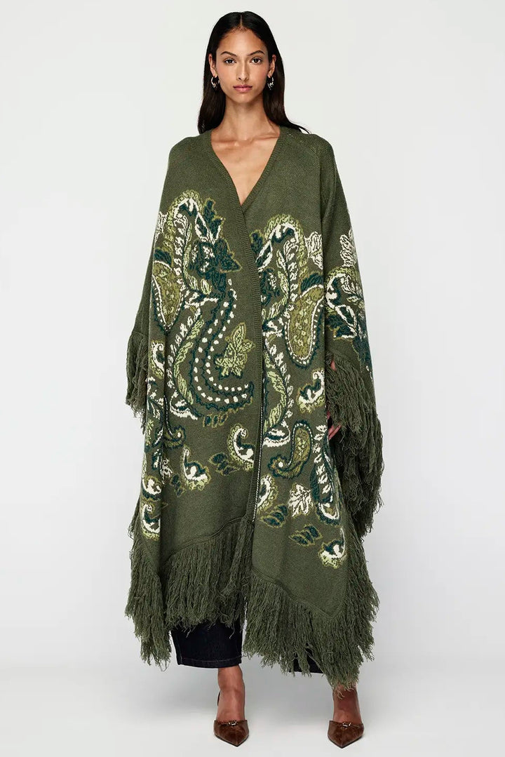 Woman wearing a green embroidered poncho with fringe on a white background