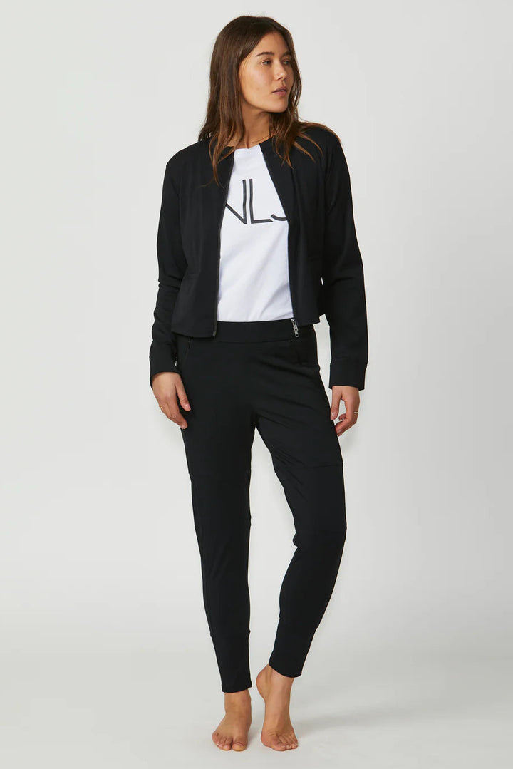 Woman wearing a black blazer, white t-shirt with a logo, and black pants on a white background