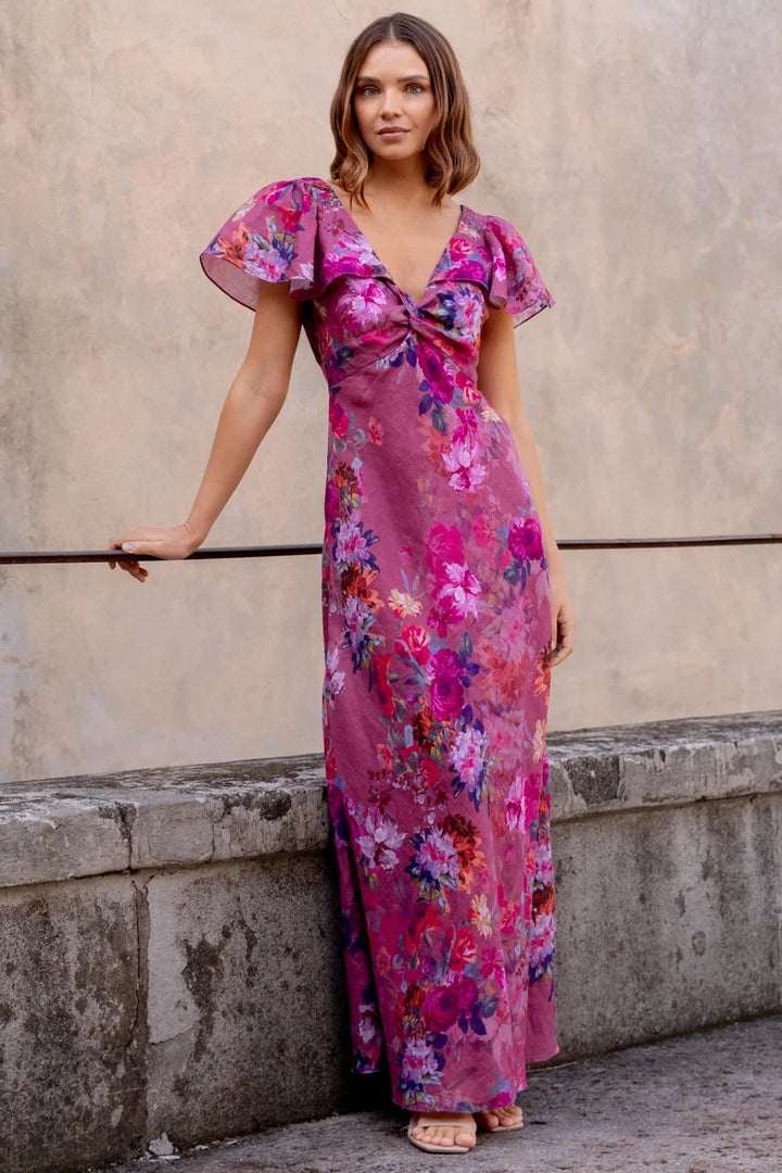 Woman in a floral dress standing against a stone wall.