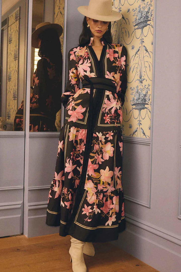 Woman in a floral dress standing in front of a mirror with decorative wallpaper.
