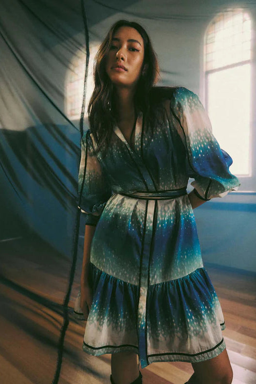 A woman wearing a short shirt dress with a galaxy print, featuring a blue, white, and black color scheme, with soft blouson sleeves and a knee-length silhouette.