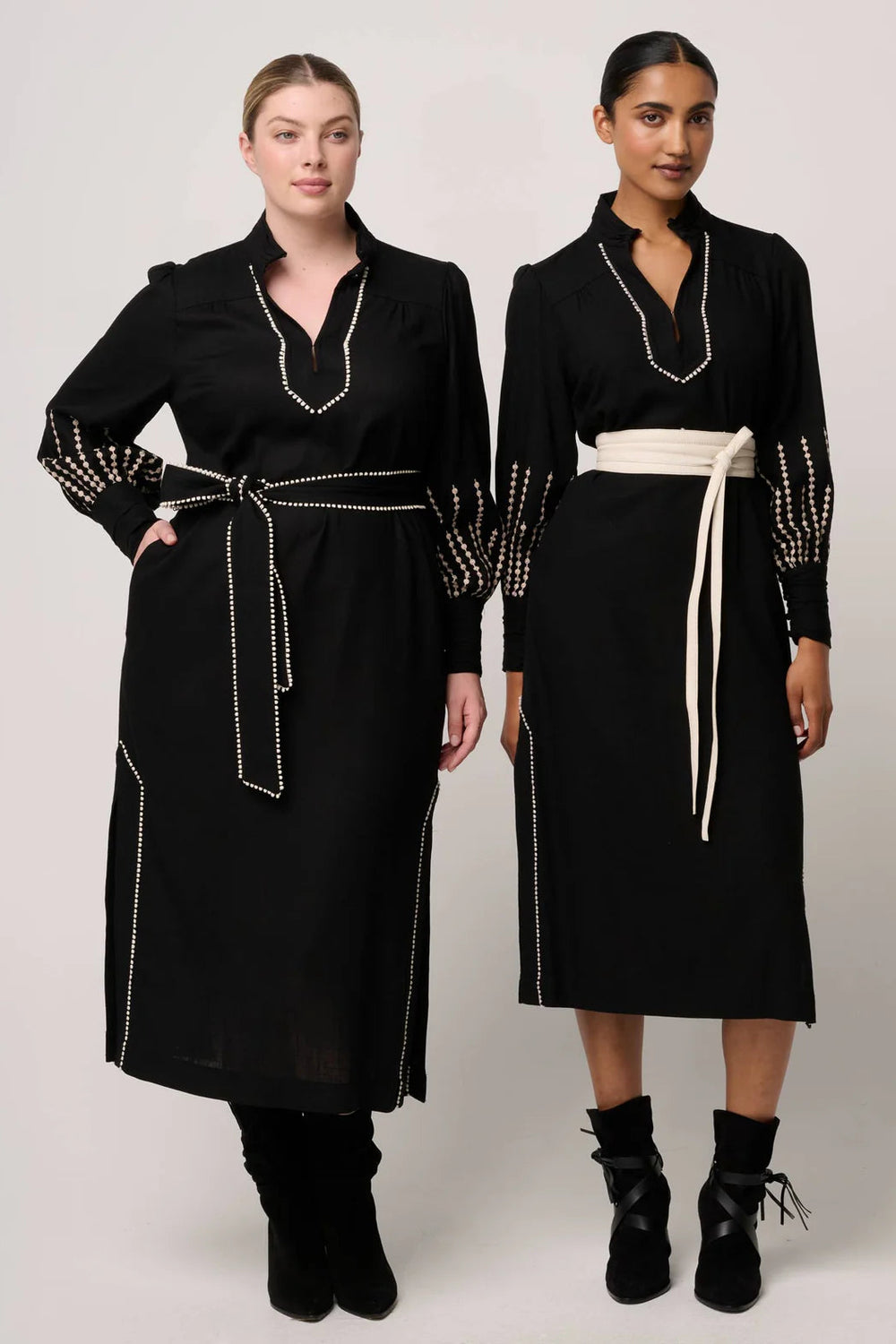 Two women wearing black dresses with decorative elements on a plain background