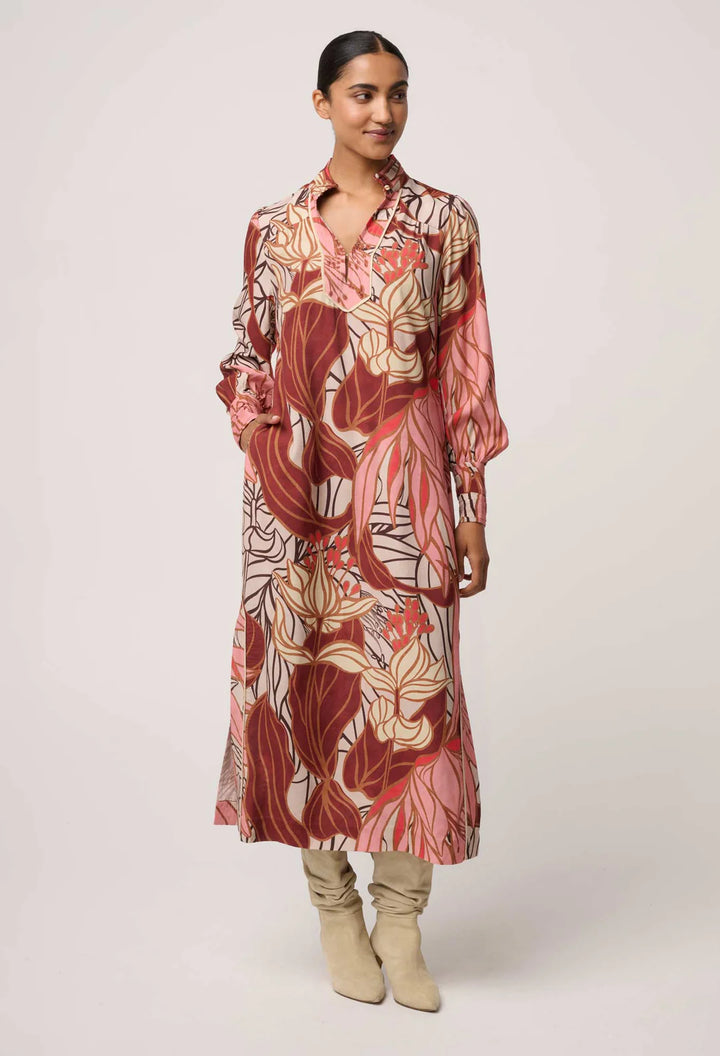 Woman wearing a long, patterned dress with beige boots on a white background