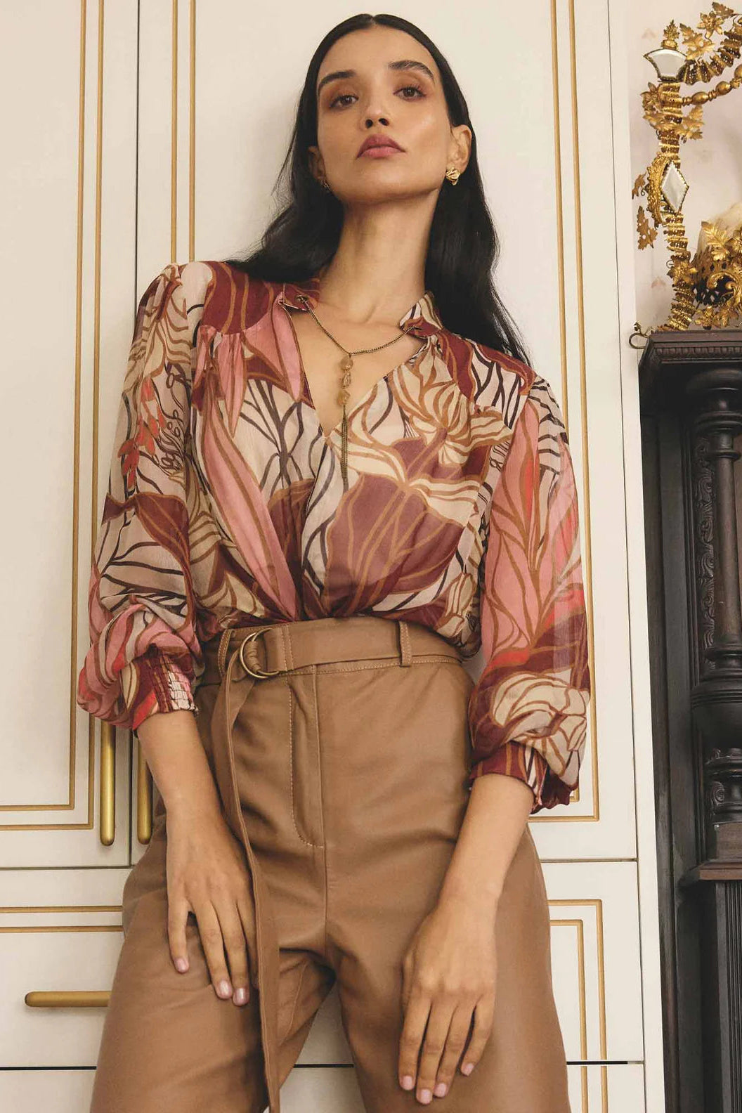 Woman wearing a patterned blouse and beige pants in an elegant interior setting