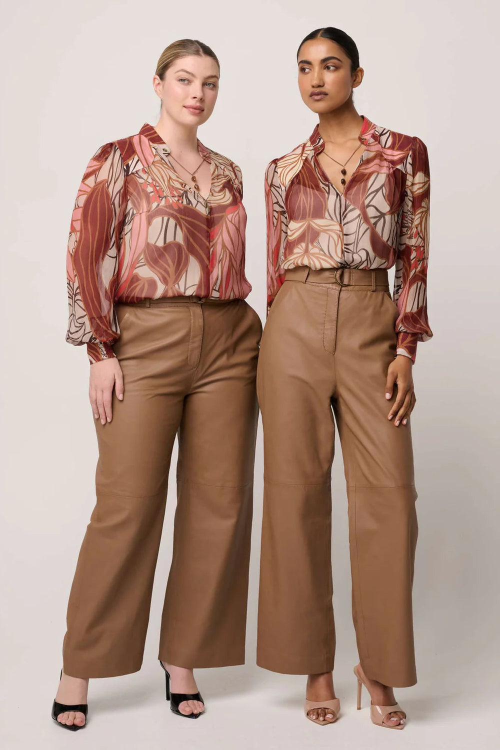 Two women wearing matching outfits with floral tops and brown pants on a white background