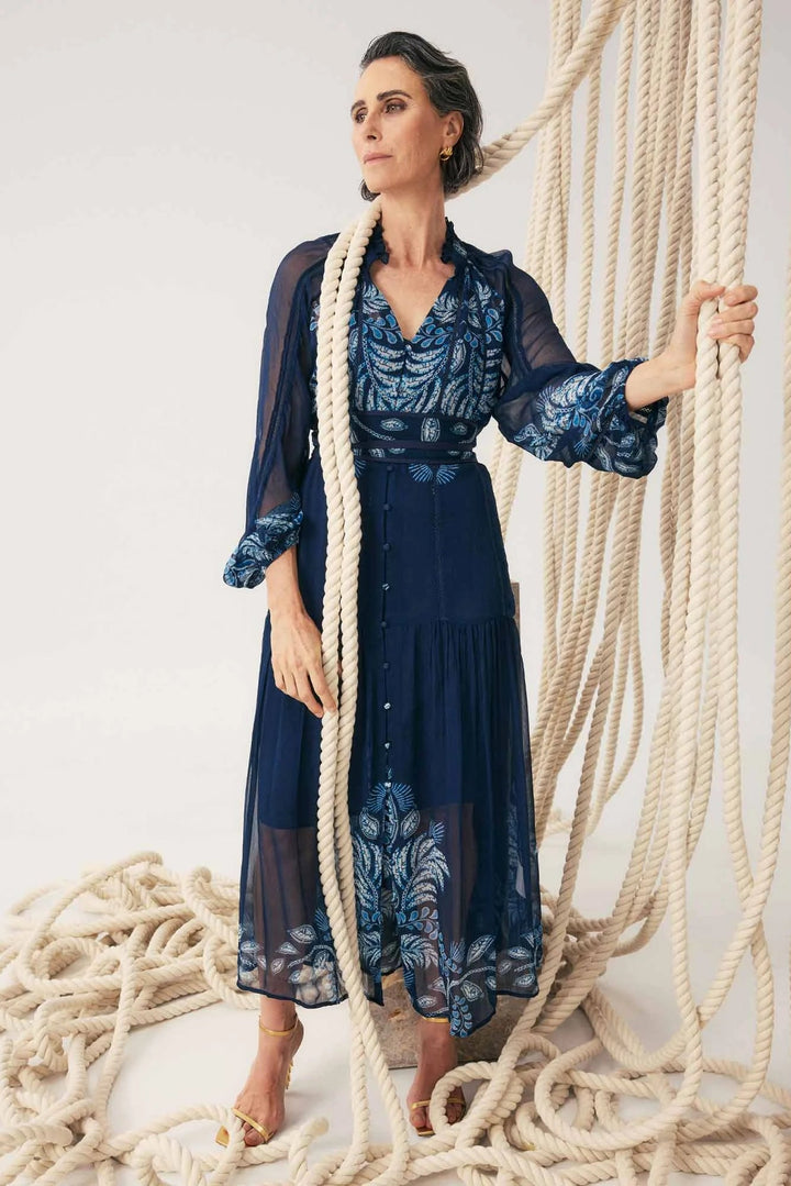 Woman in a blue dress standing among large ropes on a white background