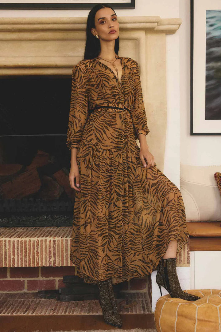 Woman in a patterned dress standing in a room with a fireplace and artwork.