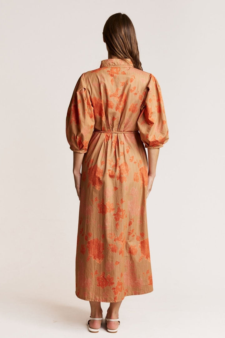 Woman wearing a long, patterned dress with orange and red floral design on a plain background