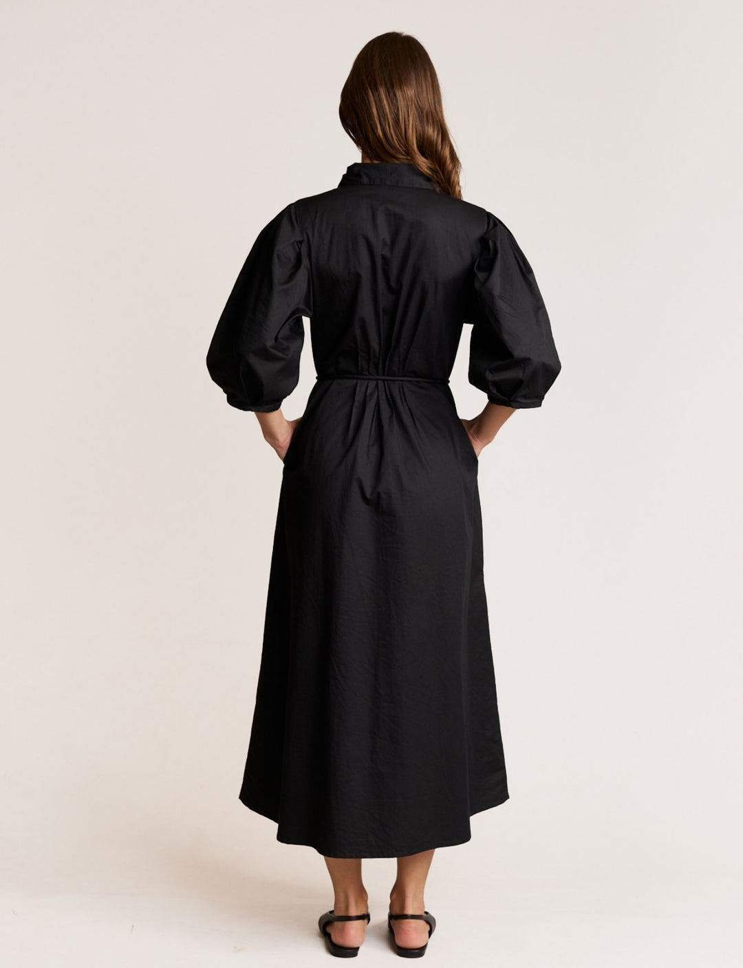 Woman wearing a black dress with puffed sleeves on a plain background