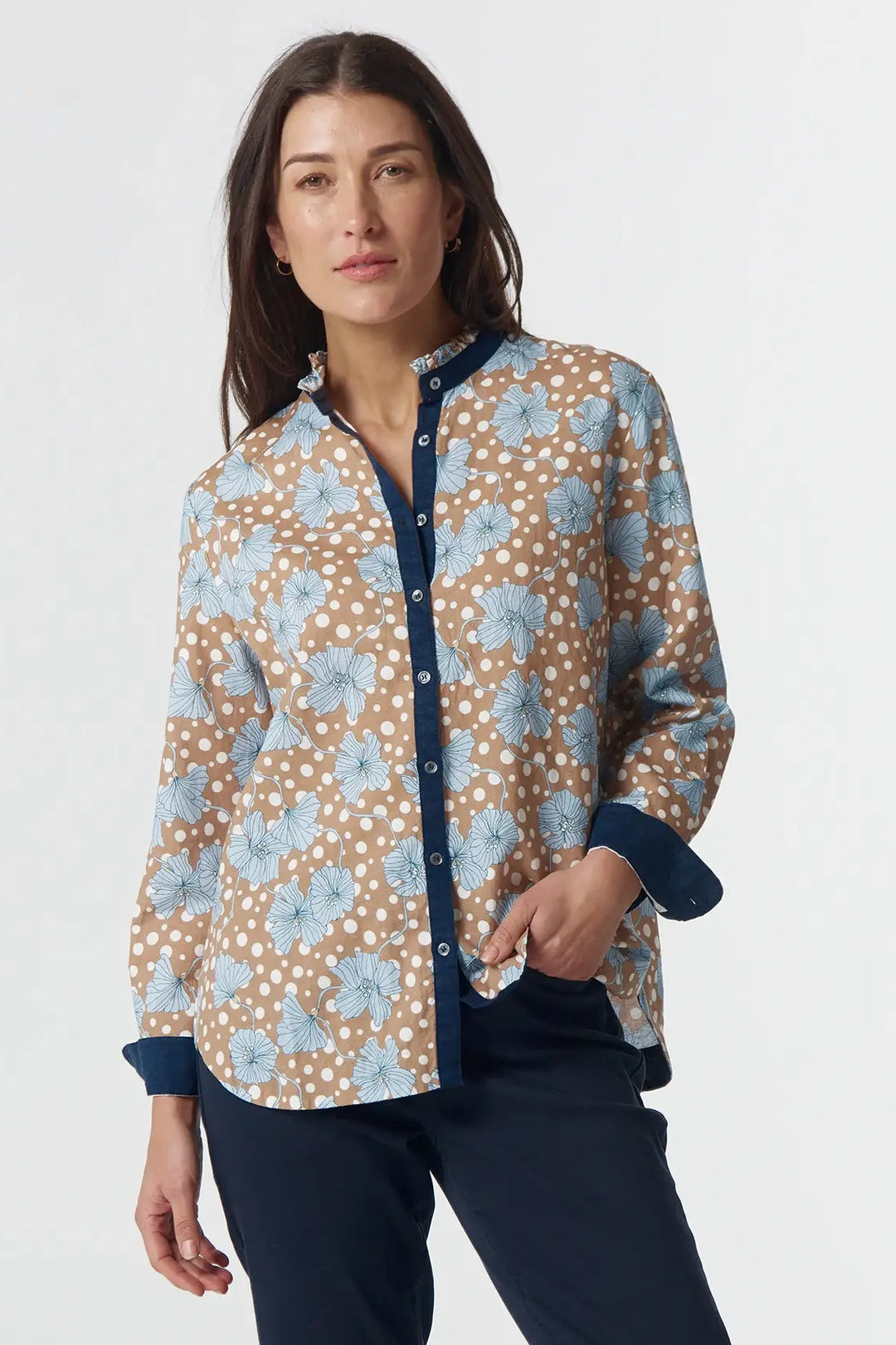 Woman wearing a patterned shirt and navy pants on a white background