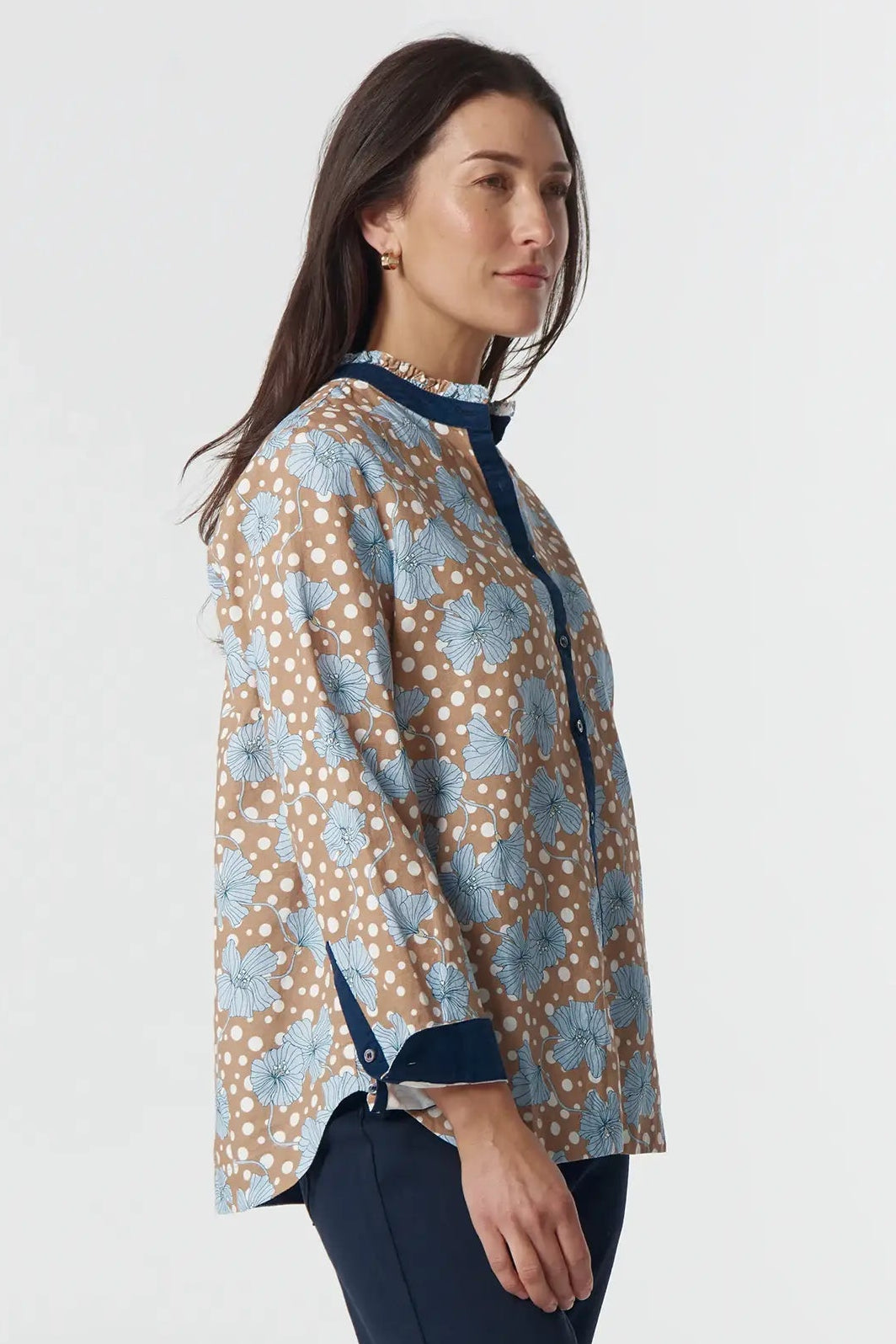 Woman wearing a patterned blouse and navy pants on a white background