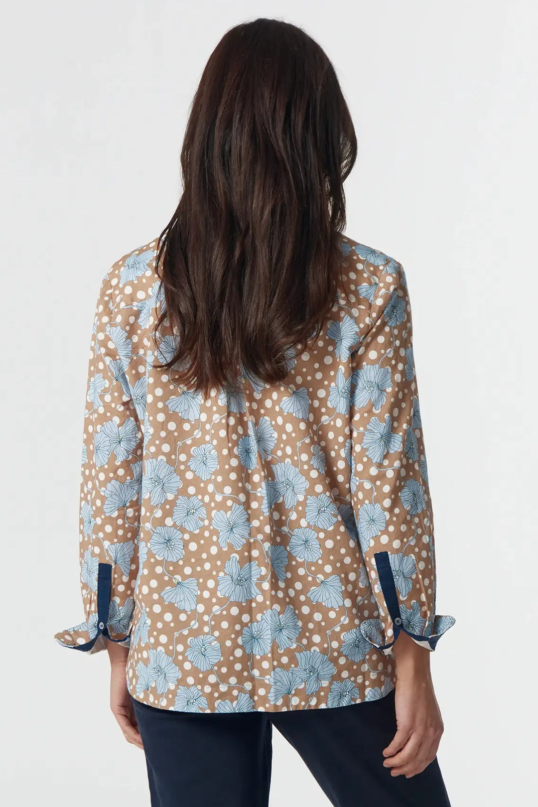Woman wearing a patterned blouse and navy pants on a white background