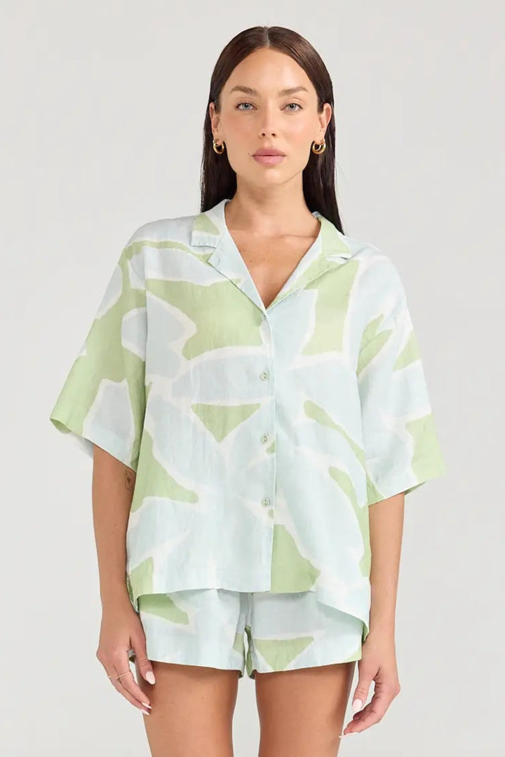 Woman wearing a light green and white patterned shirt and shorts on a plain background