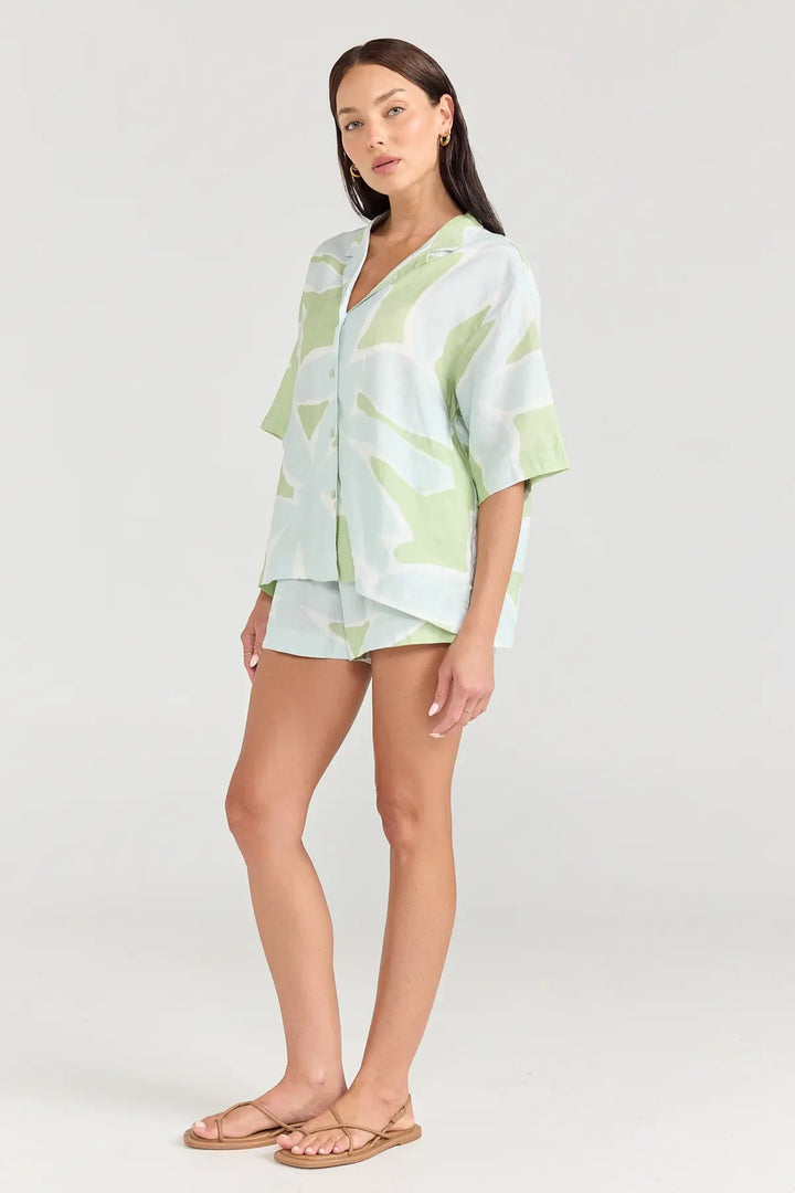 Woman wearing a light green and white patterned outfit on a plain background