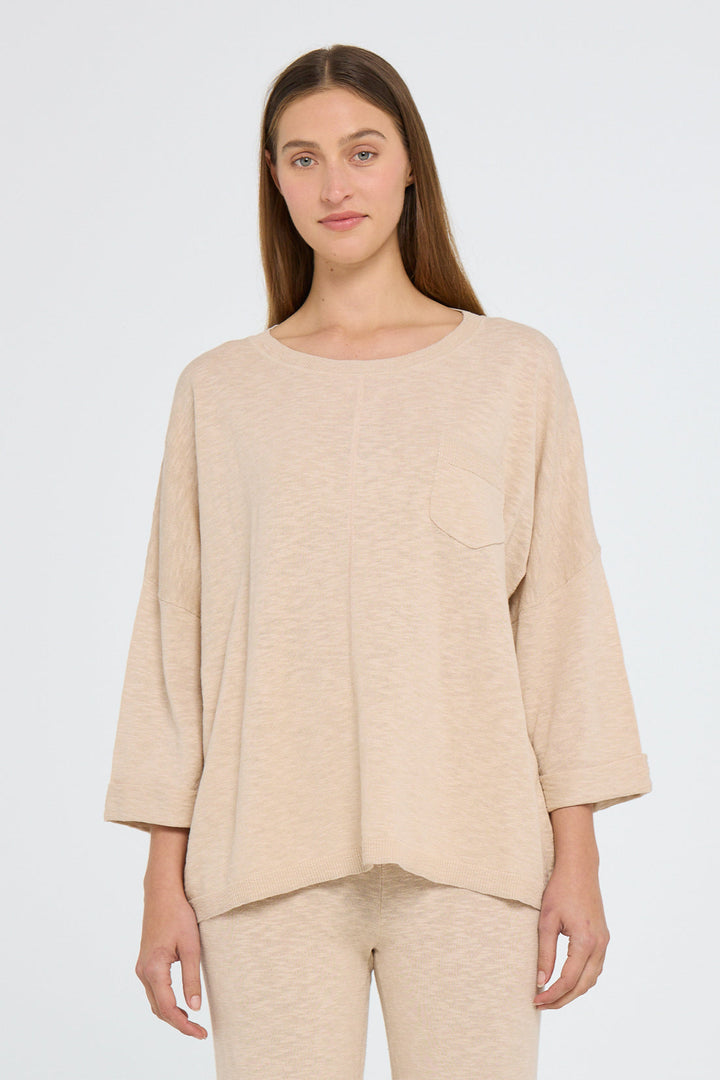 A woman wearing a beige round neck, 3/4 sleeve top with a ribbed texture.