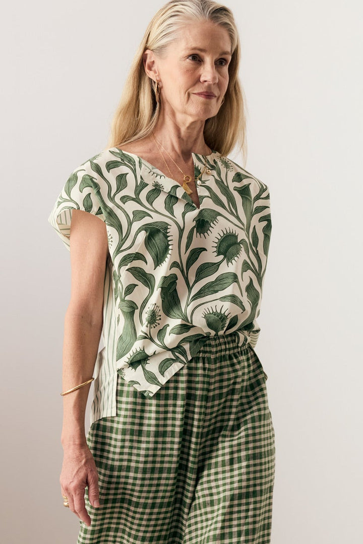 A woman modeling a matching two-piece outfit featuring a green and white tropical leaf print short-sleeve top and matching green and white gingham wide-leg pants, paired with black strappy sandals.