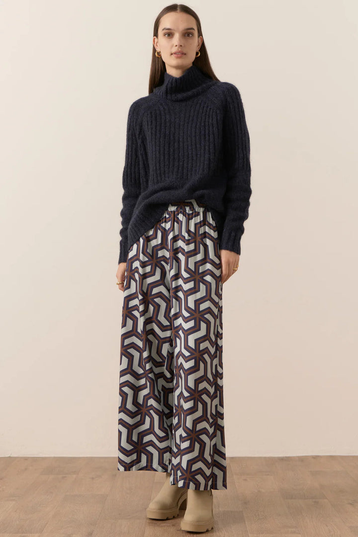 Woman wearing a dark sweater and patterned skirt against a plain background