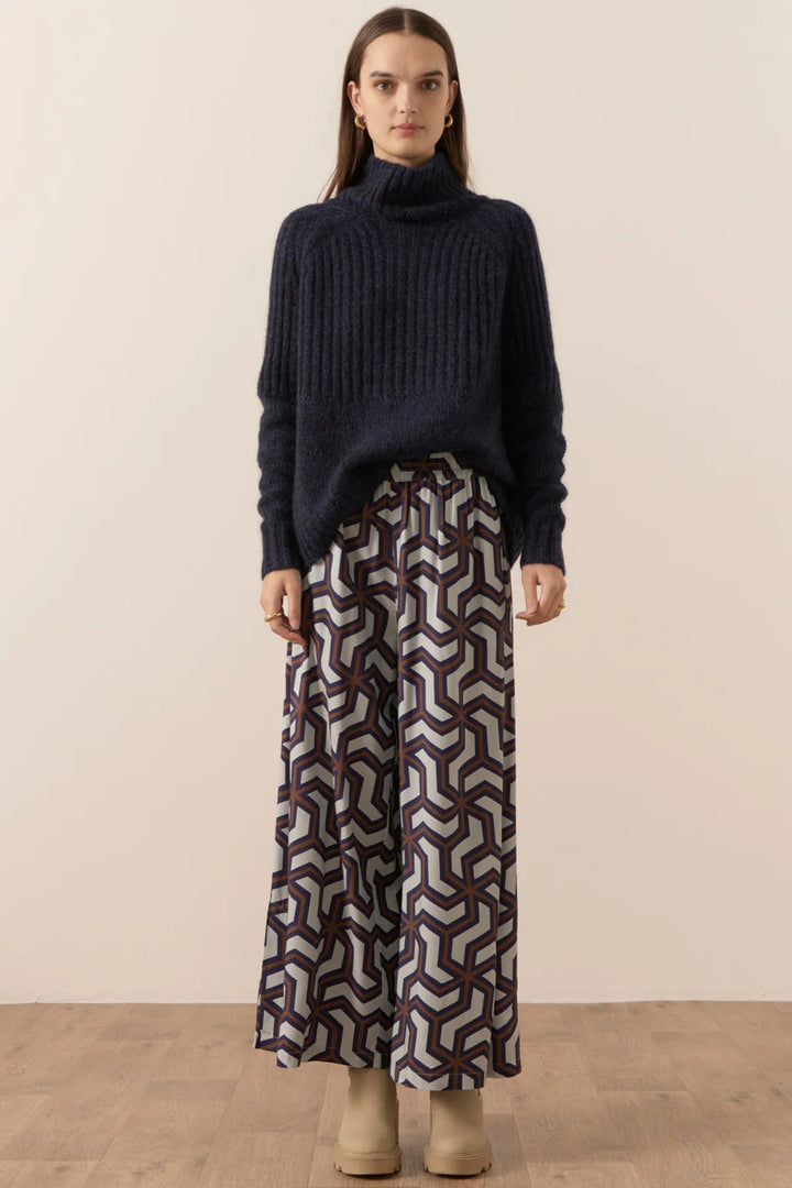 Woman wearing a dark blue sweater and patterned pants against a beige background