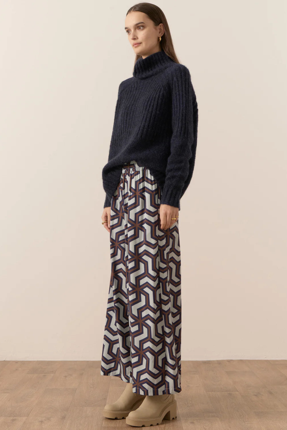 Woman wearing a dark sweater and patterned pants on a plain background